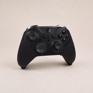 Op de afbeelding: Een matzwarte draadloze videogamecontroller met twee asymmetrische analoge sticks, een richtingspad, vier actieknoppen gelabeld A, B, X en Y, een centrale Xbox-logoknop en extra menu- en weergaveknoppen aan de voorzijde van het apparaat.