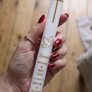 Puede incluir: Una vela blanca cónica con una cruz dorada y un gráfico de paloma. El texto dice: Ronan, NAISSANCE 28 MARS 2025, BAPTEME 20 SEPTEMBRE 2026. La vela tiene un acabado liso y una parte superior puntiaguda, diseñada para uso ceremonial.
