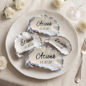 May include: Four white oyster shells with silver-painted edges, each featuring black printed text. Three shells display the name Ationk or Etionk with the date 12.20.26, while one smaller shell displays the name Dtiomka with the date 12.20.26.