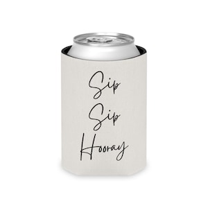Puede incluir: Un enfriador de latas blanco con las palabras "Sip Sip Hooray" en escritura negra. El enfriador envuelve una lata plateada. El diseño es simple y sugiere un tema festivo, ideal para fiestas.