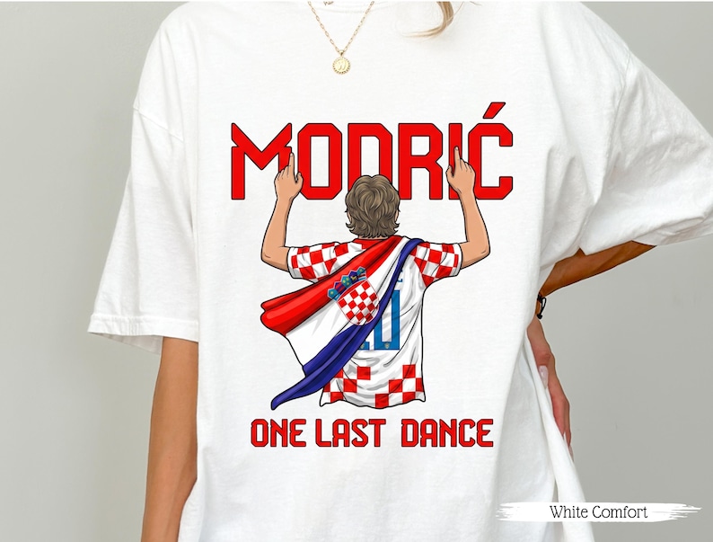 May include: White t-shirt featuring a graphic of a soccer player wearing a Croatian flag. The word "MODRIĆ" is in red block letters above the player, with the text "ONE LAST DANCE" below. The shirt is labeled "White Comfort".