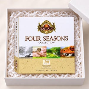 Może przedstawiać: Kwadratowe pudełko herbaty Basilur Four Seasons Collection zawierające 40 różnych torebek herbaty. Białe pudełko posiada złote logo, napis Four Seasons Collection oraz cztery obrazy krajobrazów przedstawiające herbaty zimowe, wiosenne, letnie i jesienne.