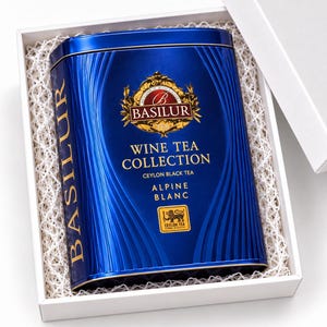 以下が含まれることがあります： Basilur Wine Tea Collection Alpine Blancと書かれた青い長方形の金属製紅茶缶。ライオンのロゴと金色の文字が特徴で、白いギフトボックスの中に白い紙の緩衝材と共に収められています。缶には縦方向のエンボス加工が施されています。