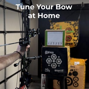 May include: A compound bow is aimed at a target in a home setting. The text "Tune Your Bow at Home" is displayed at the top. The target is a black and white archery target with a green and brown box on top.