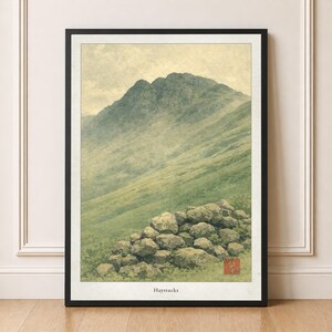 May include: Framed art print of a mountain landscape. The print features a green hillside, a stone wall, and a mountain peak. The title "Haystacks" is printed at the bottom. A red square with Japanese characters is in the lower right corner.