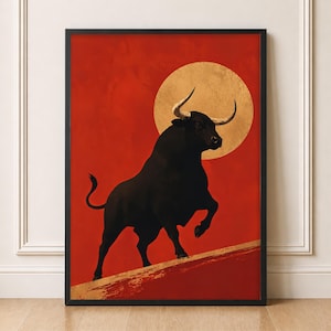 May include: A framed wall art print featuring a black bull standing on a textured gold diagonal line against a solid red background. A large, circular gold sun or moon shape is positioned behind the bull, which has curved, light-colored horns.