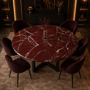 Op de afbeelding: Een ronde eettafel met een dieprood marmeren blad met witte aders, ondersteund door een zwart metalen onderstel. Zes bijpassende donkerbordeauxrode fluwelen stoelen met verticale stiksels zijn rondom de tafel geplaatst.
