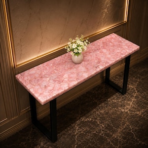 May include: A rectangular pink quartz console table with a black metal frame. The table features a mosaic-like surface and is topped with a small vase of white flowers. The table is approximately 48 inches long.