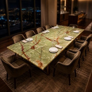 Op de afbeelding: Een rechthoekige eettafel met een gepolijst groen onyx stenen blad met opvallende bruine aders. De tafel is omringd door tien gestoffeerde fauteuils in een gedempte bruine tint, elk gedekt met een wit bord, een glas en een servet.