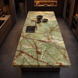May include: A large rectangular kitchen island featuring a polished green onyx countertop with prominent rust-coloured veining. The island includes a rectangular stainless steel sink with a black faucet, two dark bowls, and two clear glass wine glasses.