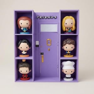 May include: A purple display cabinet with six character figurines from the TV show "Friends." The cabinet has a central door with the show's logo above. Each figurine is on a shelf, with the characters in different outfits.