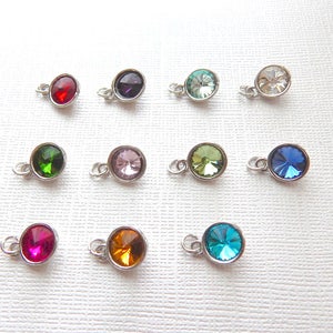 May include: Twelve silver charms with different colored rhinestones. The charms are round and have a loop at the top for attaching to a bracelet or necklace.