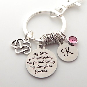May include: Silver keychain with a charm that reads "my little girl yesterday, my friend today, my daughter forever". The keychain also has a charm with the letter "K" and a pink crystal.