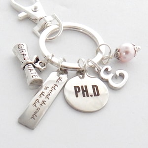 May include: Silver keychain with a graduation cap charm, a charm that says "The future is so bright we gotta wear shades", a charm that says "PH.D", a charm with the number 3, and a pink pearl charm.
