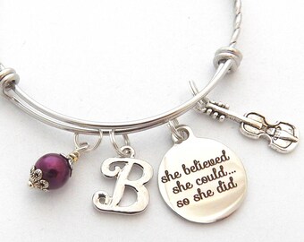 May include: Silver expandable bracelet with a purple bead, a charm with the letter "B", and a charm with the text "She believed she could... so she did".