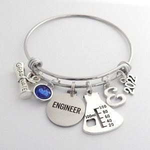 May include: Silver charm bracelet with graduation cap, blue crystal, "Engineer" charm, beaker charm, "Class of 2022" charm, and a letter "G" charm.