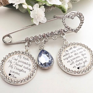 May include: A silver safety pin with a heart-shaped charm and two round charms. The charms are decorated with rhinestones and have the following text: "My little Girl yesterday My Friend today My Daughter forever. Mom" and "Of all the walks we've taken together, this one is my favorite. You will always be my little girl. Dad"