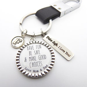 May include: Silver keychain with a round charm that says "Have Fun Be Safe & Make Good Choices Love Mom & Dad". A smaller charm with the letter "F" hangs from the keychain. A silver tag with the text "Drive Safe. I Love You" is attached to the keychain.