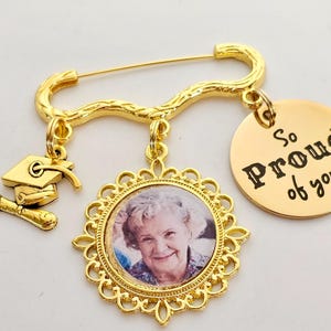 May include: Gold graduation pin with a photo charm, a graduation cap charm, and a round charm that says "So Proud of You".