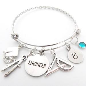 May include: Silver charm bracelet with charms including a graduation cap, compass, protractor, a charm with the word "ENGINEER" and a charm with the letter "E".
