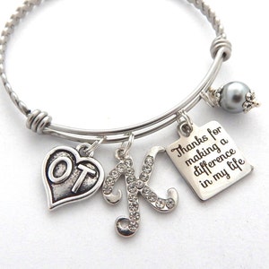 May include: Silver charm bracelet with a heart charm that says "OT", a charm with the letter "K" set with rhinestones, and a square charm that says "Thanks for making a difference in my life".