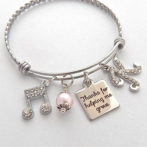 Peut inclure: Bracelet en argent avec un charme de perle rose, un charme de note de musique, un charme carr&eacute; avec le texte "Merci de m'aider &agrave; grandir" et un charme lettre K. Le bracelet est fait de fil d'argent torsad&eacute;.