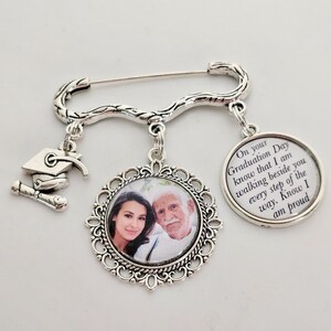 May include: Silver graduation pin with a photo charm, a graduation cap charm, and a charm with the text "On your Graduation Day know that I am walking beside you every step of the way. Know I am proud."