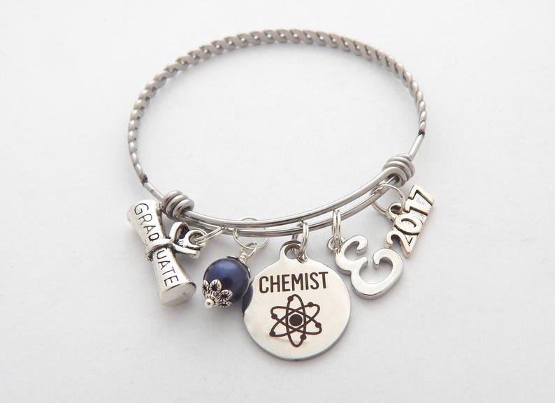 May include: Silver charm bracelet with graduation cap, 'Graduate', '2017', 'C', and 'Chemist' charms. The 'Chemist' charm features an atom symbol.