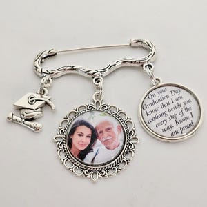 May include: Silver graduation pin with a photo charm, a graduation cap charm, and a charm with the text "On your Graduation Day know that I am walking beside you every step of the way. Know I am proud."