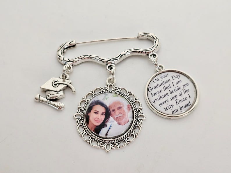 May include: Silver graduation pin with a photo charm, a graduation cap charm, and a charm with the text "On your Graduation Day know that I am walking beside you every step of the way. Know I am proud."