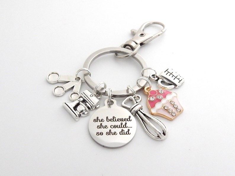 May include: Silver keychain with charms including a cupcake, measuring cups, a whisk, a mixer, and a round tag that reads "she believed she could... so she did".