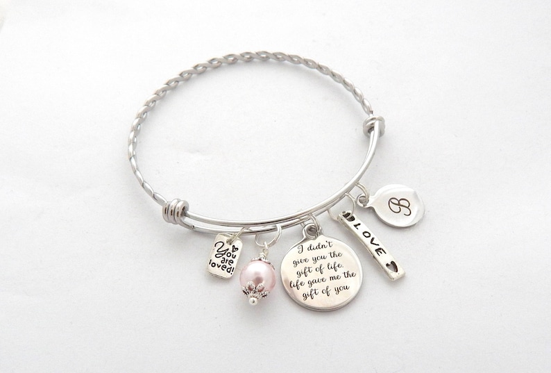 May include: A silver charm bracelet with a pink pearl charm, a charm that says "You are loved!" and a charm that says "I didn't give you the gift of life, life gave me the gift of you". The bracelet also has a charm with the letter "B" and a charm that says "LOVE" with a heart.