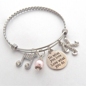 Puede incluir: Pulsera de plata con un encanto de perla rosa, un encanto de nota musical y un encanto con el texto "Do what you love Love what you do".