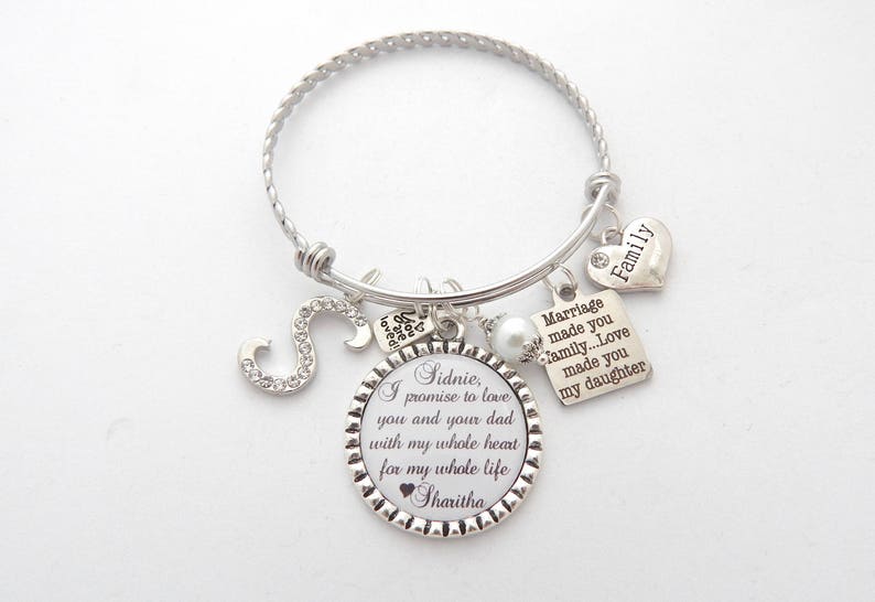 May include: Silver charm bracelet with a round charm that says "Sidnie, I promise to love you and your dad with my whole heart for my whole life Sharitha". The bracelet also has charms that say "Family", "Marriage made you family...Love made you my daughter", and a letter "S" charm.