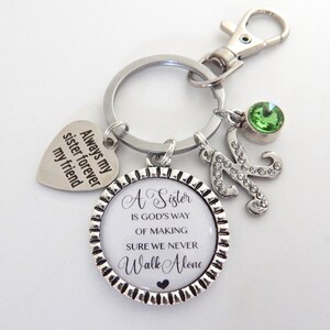 K&ouml;nnte beinhalten: Silberner Schl&uuml;sselanh&auml;nger mit einem Herz-Anh&auml;nger, auf dem "Always my sister forever my friend" steht, und einem runden Anh&auml;nger, auf dem "A Sister is God's way of making sure we never walk alone" steht. Der Schl&uuml;sselanh&auml;nger hat au&szlig;erdem einen gr&uuml;nen Strassstein und einen silbernen Anh&auml;nger mit dem Buchstaben K.