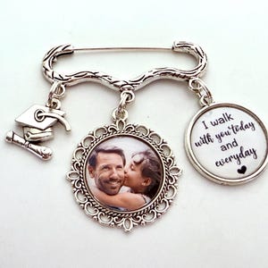 May include: Silver brooch with a graduation cap charm, a photo charm of a couple, and a charm with the text "I walk with you today and everyday".