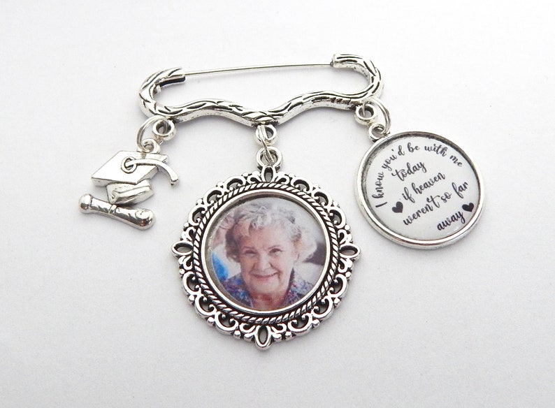 May include: Silver graduation pin with a photo charm, a graduation cap charm, and a charm with the text "I know you'd be with me today if heaven weren't so far away".