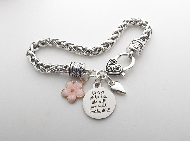 Puede incluir: Pulsera de cadena plateada con un dije de coraz&oacute;n, un dije de flor rosa y un dije redondo con el texto "Dios est&aacute; en ella, no caer&aacute;. Salmo 46:5".