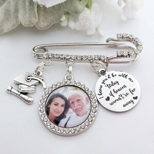 May include: Silver safety pin with a photo charm, a graduation cap charm, and a charm with the text "I know you'd be with me today if heaven weren't so far away".