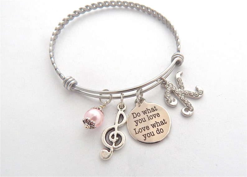 Peut inclure: Un bracelet argent&eacute; avec un charme qui dit "Do what you love Love what you do" et un charme avec une note de musique. Le bracelet a &eacute;galement un charme de perle rose et un charme avec la lettre K d&eacute;cor&eacute;e de strass.