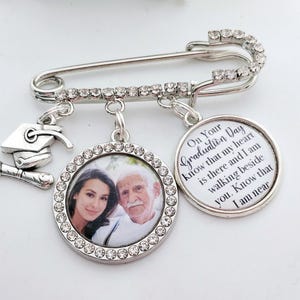 May include: Silver graduation pin with a photo charm, a graduation cap charm, and a charm with the text "On Your Graduation Day know that my heart is there and I am walking beside you. Know that I am near."