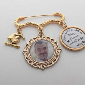 May include: Gold tone memorial brooch with a photo charm, a graduation cap charm, and a round charm with the text "I knew you'd be with me today if heaven weren't so far away".