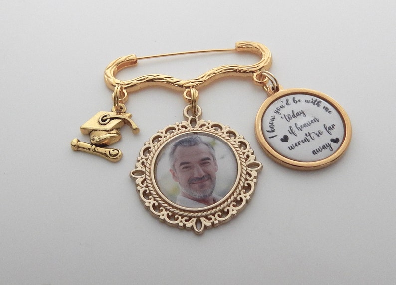 May include: Gold tone memorial brooch with a photo charm, a graduation cap charm, and a round charm with the text "I knew you'd be with me today if heaven weren't so far away".