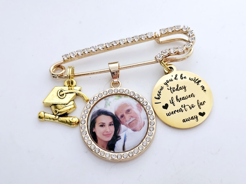 May include: Gold graduation pin with a photo charm, a graduation cap charm, and a charm with the text "I know you'd be with me today if heaven weren't so far away".