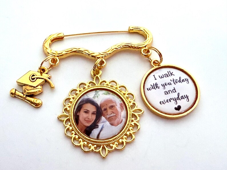 May include: Gold-toned brooch with a photo charm, a graduation cap charm, and a charm with the text "I walk with you today and everyday".