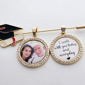 May include: Gold graduation pin with a black graduation cap and a white scroll. The pin has two round charms, one with a photo of a man and woman, and the other with the text "I walk with you today and everyday" with a small heart.