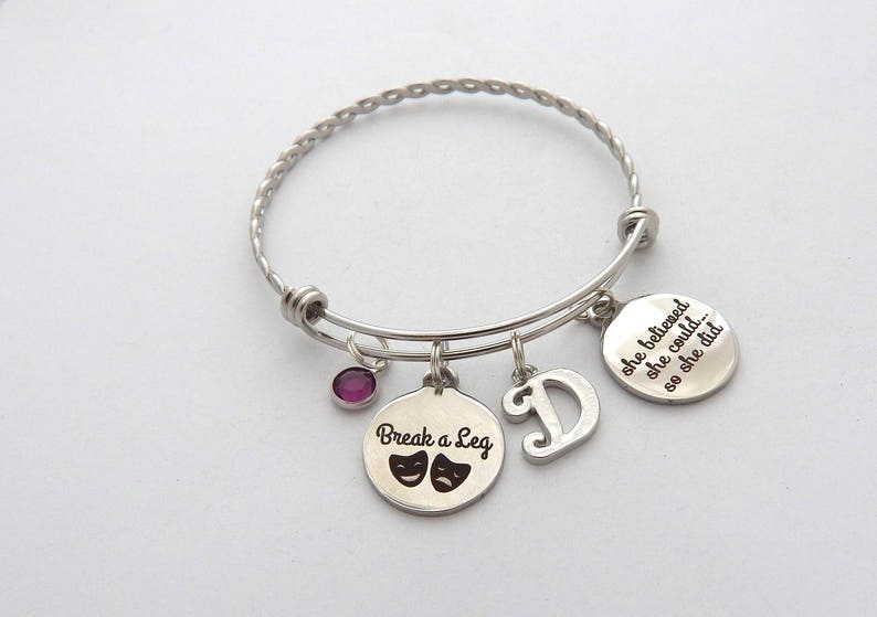 May include: Silver charm bracelet with four charms. The charms say "Break a Leg" with two theater masks, "D", and "She believed she could... so she did."