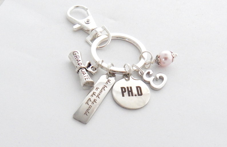 May include: Silver keychain with a graduation cap charm, a charm that says "The future is so bright we gotta wear shades", a charm that says "PH.D", a charm with the number 3, and a pink pearl charm.