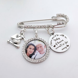 May include: Silver graduation pin with a photo charm, a graduation cap charm, and a charm with the text "I know you'd be with me today if heaven weren't so far away".