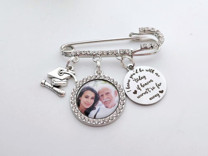 May include: Silver graduation pin with a photo charm, a graduation cap charm, and a charm with the text "I know you'd be with me today if heaven weren't so far away".